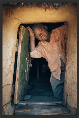 Een jongen kijkt voorzichtig naar buiten vanuit een oude, halfopen deur.