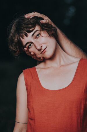 Een jonge vrouw met korte, krullende haren draagt een rode top, met een hand die haar hoofd aanraakt.