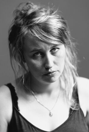 Portret van een vrouw met een serieus gezicht, lang haar en een eenvoudige top, gefotografeerd in zwart-wit.