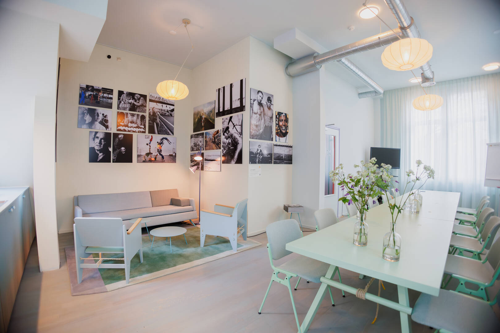 Moderne, lichte vergaderruimte met een houten tafel, stoelen en kunst aan de muur. Planten en sfeerverlichting zijn aanwezig.