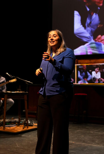 Spreker op het podium tijdens een presentatie, met een projectie op de achtergrond.