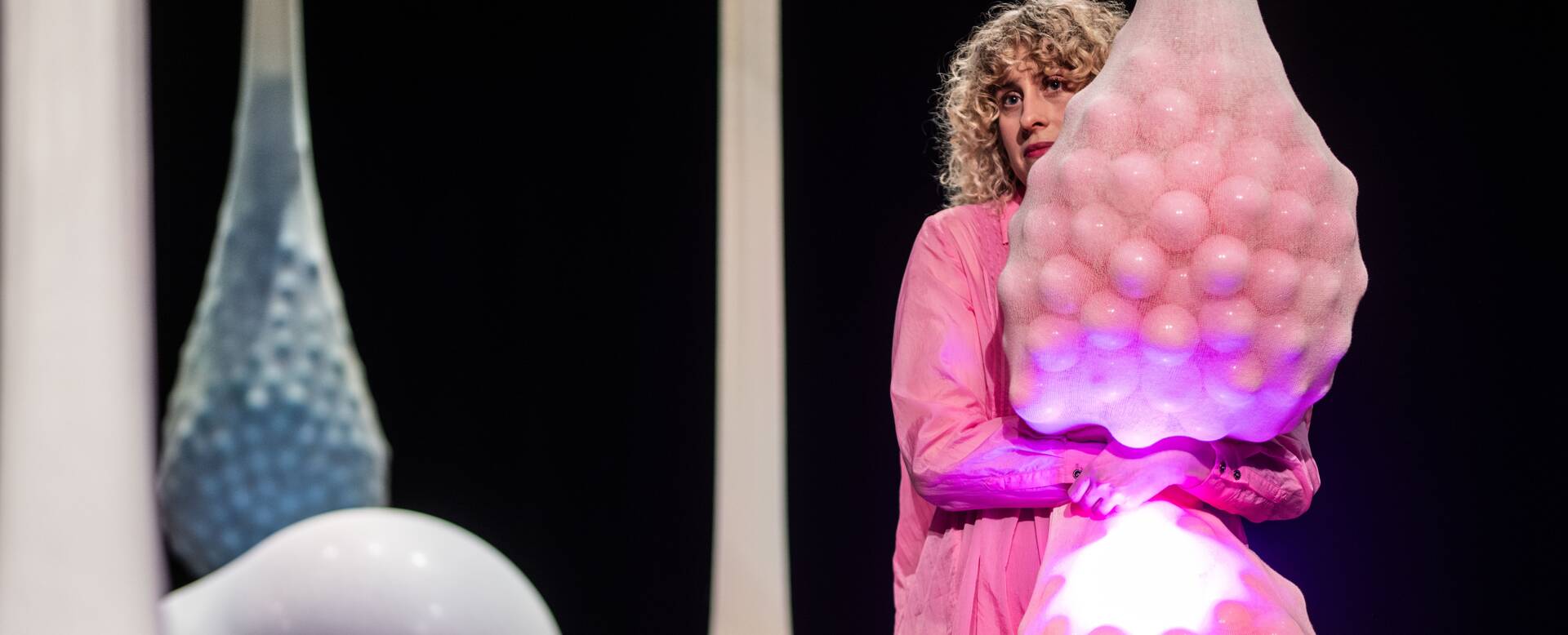 Een persoon in een roze outfit houdt een grote, decoratieve sculptuur vast, met een abstracte, organische vorm.