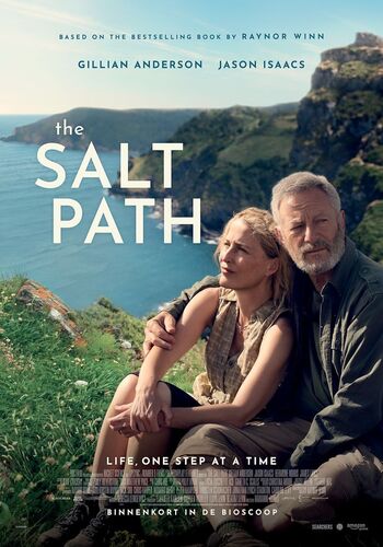 Filmposters van "The Salt Path" met hoofdpersonages Gillian Anderson en Jason Isaacs op een groene heuvel met uitzicht op zee.