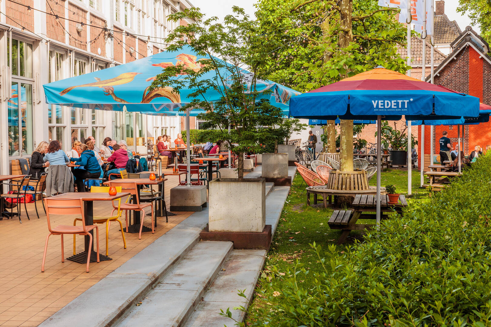 Gezellige terrasomgeving met kleurrijke parasols en mensen die ontspannen genieten van hun tijd.