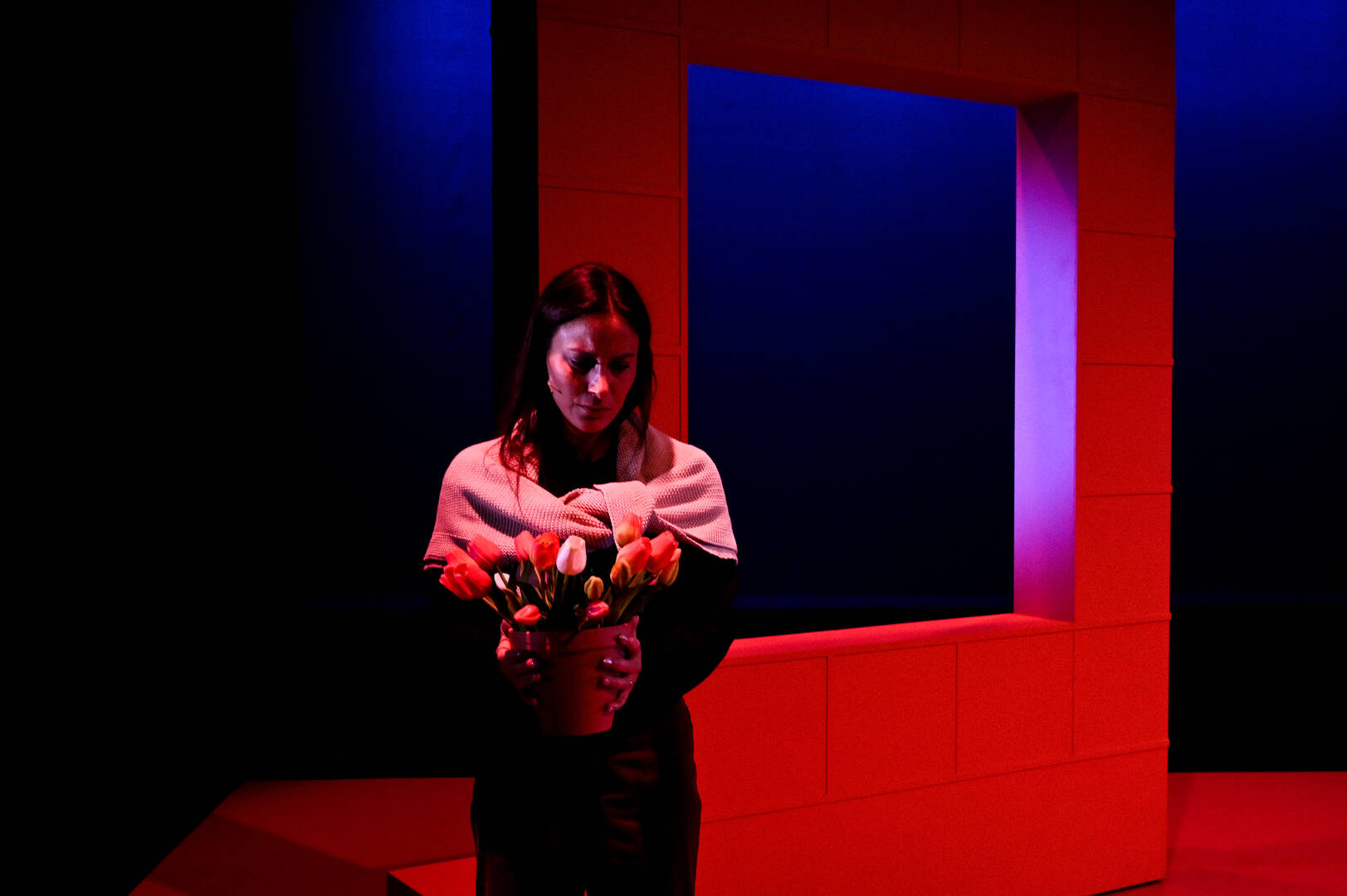 Een vrouw in een donkere ruimte met blauwe en rode verlichting, houdt een boeket bloemen vast.