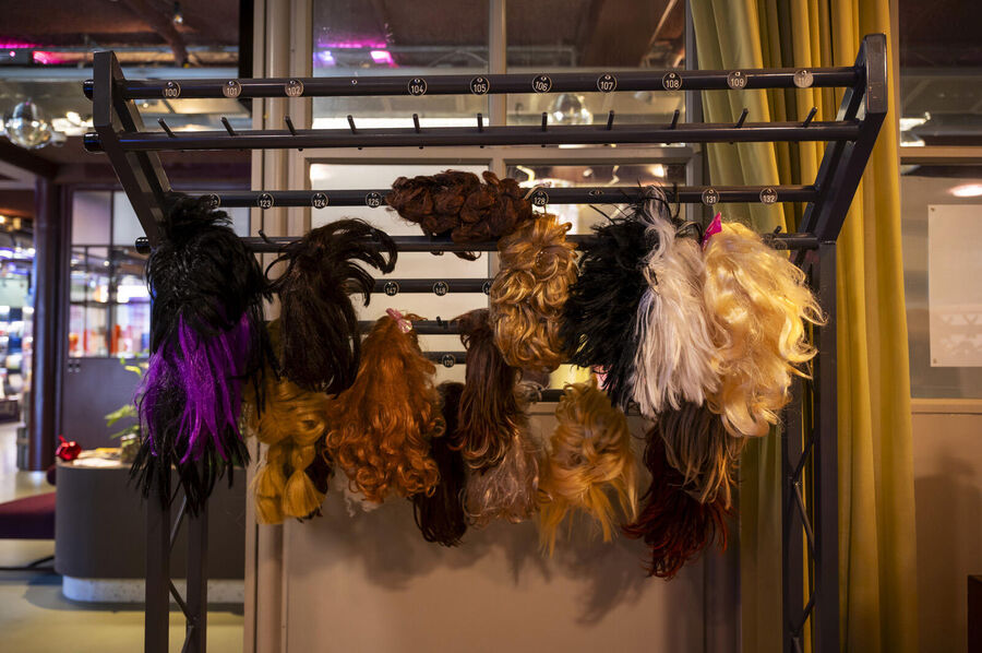 Een rek met verschillende pruiken in diverse kleuren, waaronder zwart, bruin, blond en paars.