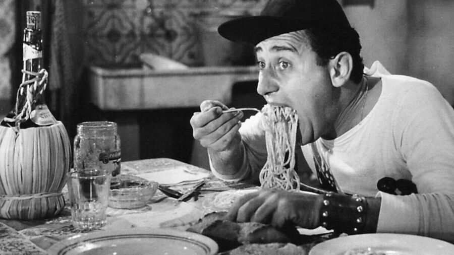 Zwart-wit afbeelding van een man die met een vork spaghetti eet aan een tafel.