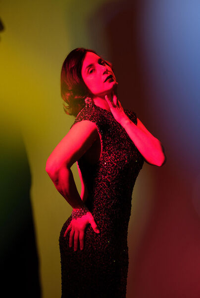 Vrouw in een glamoureuze jurk poseert met een elegante uitstraling, omringd door kleurrijke belichting.