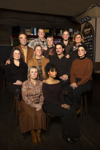 Groep mensen poseert samen in een café, glimlachend en in casual kleding.