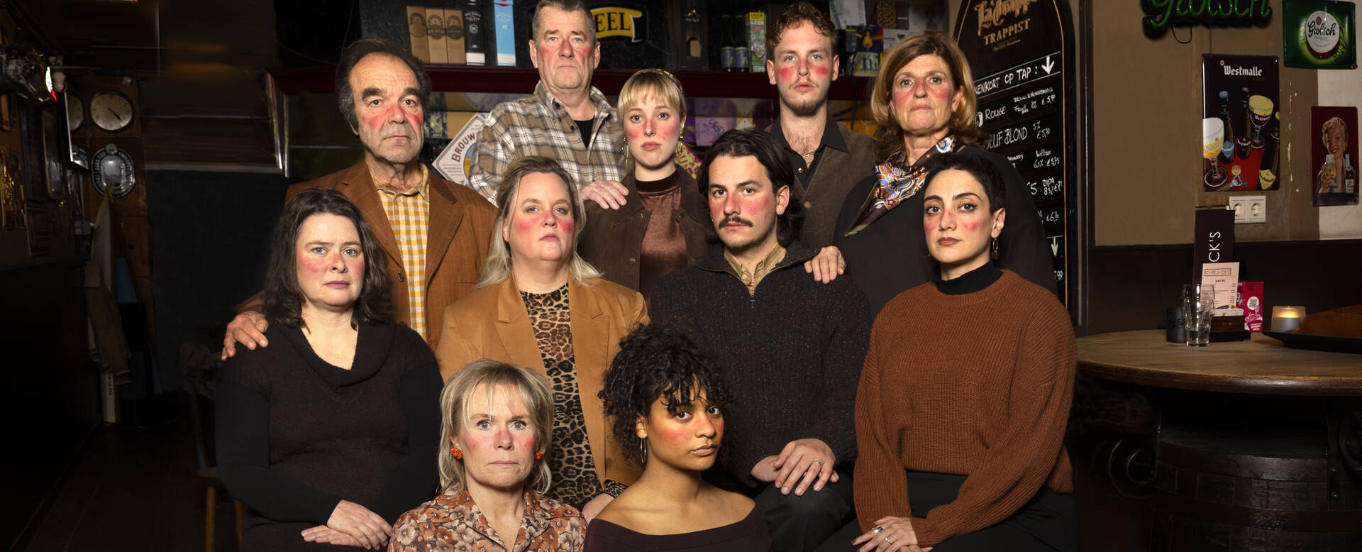 Groep van 12 mensen poseert samen in een sfeervolle binnenruimte, met verschillende outfits en expressies.