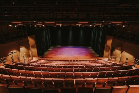Overzicht van een theaterzaal met lege stoelen en een verlichte podiumruimte.