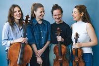 Vier vrouwen staan samen, elk met een strijkinstrument, lachend voor een blauwe achtergrond.