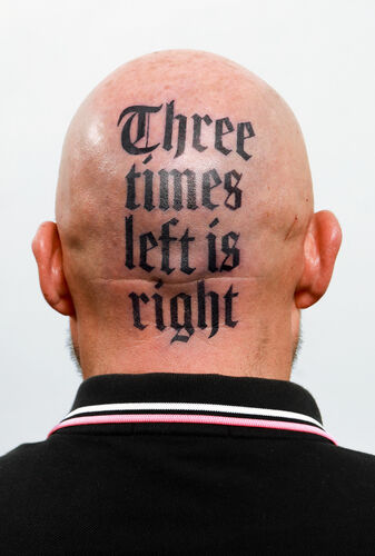 Achterkant van een kaal hoofd met een grote tattoo: "Three times left is right" in stylische letters.