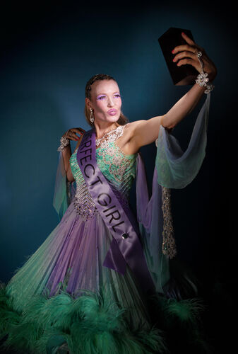 Een vrouw in een kleurrijke jurk met een sjerp poseert met een trofee in haar hand.