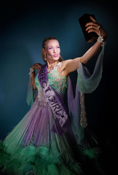 Een vrouw in een kleurrijke jurk met een sjerp poseert met een trofee in haar hand.