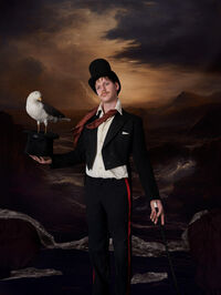 Man in een zwart kostuum met hoge hoed, houdt een vogel vast tegen een dramatische achtergrond.