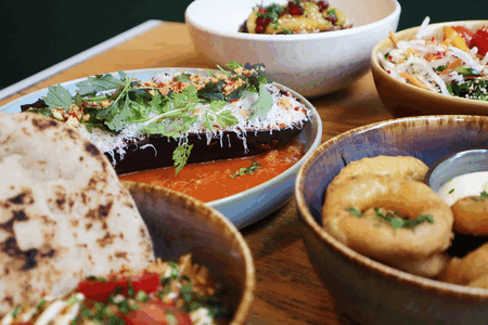 Een kleurrijk gerecht met verschillende schalen, waaronder aubergine in saus, rijst, salade en gefrituurde snacks.