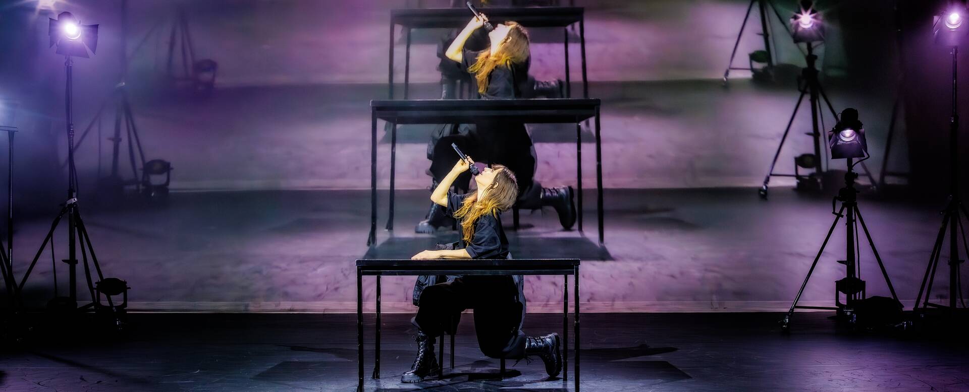Drie dansers voeren een choreografie uit op een podium met verschillende lichtbronnen.