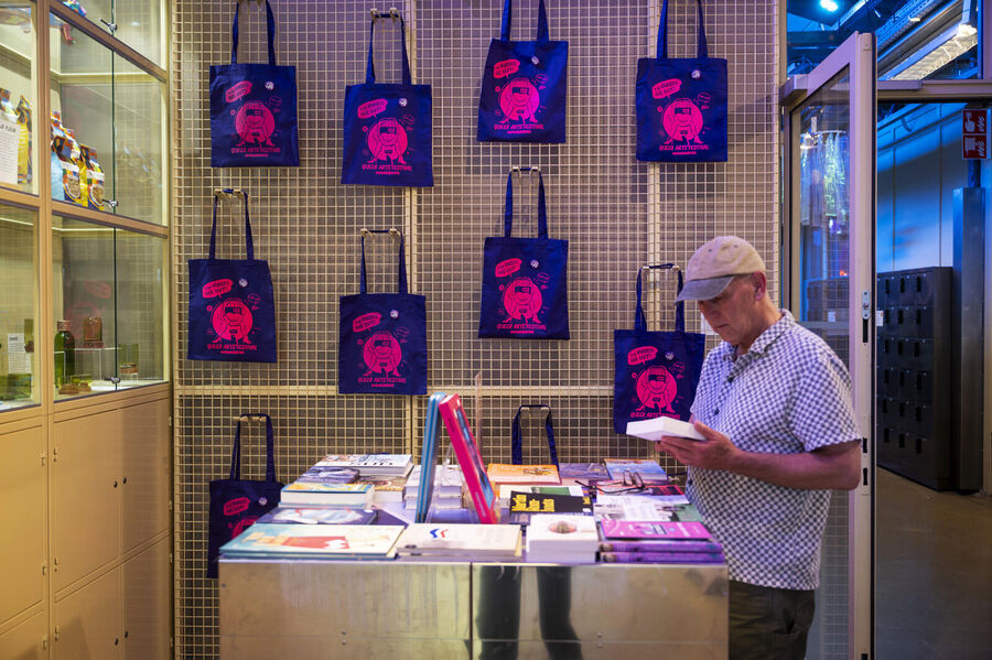 Man kijkt rond in een winkel met kleurrijke tassen en boeken op de toonbank.