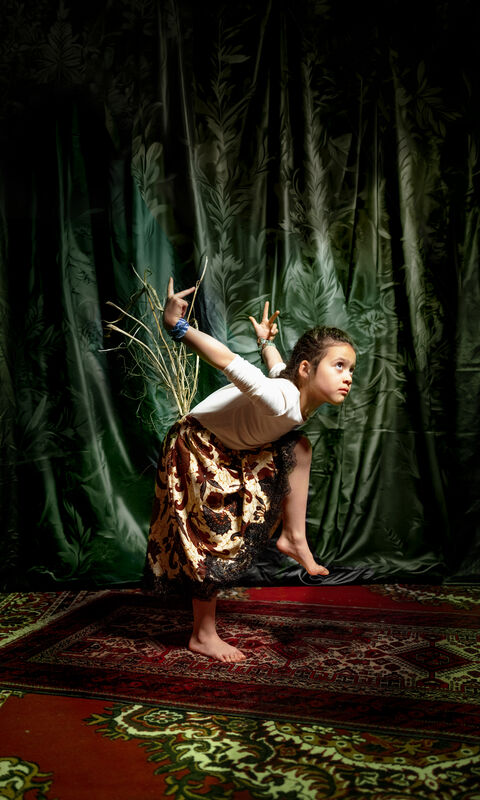 Een jonge jongen voert een acrobatische pose uit op een tapijt, met een groen fluwelen achtergrond.