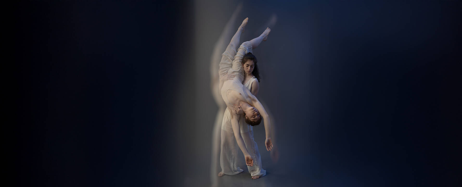 Twee dansers in elegante witte kostuums voeren een choreografie uit tegen een donkerblauwe achtergrond.