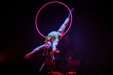 Een acrobate voert een indrukwekkende luchtperformace uit met een hoepel in een donkere setting met kleurrijke verlichting.